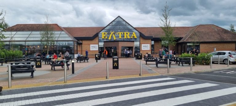 Exterior view of the beaconsfield services building with people seated at outdoor tables under cloudy skies.