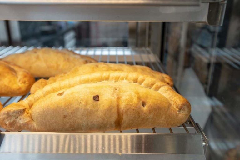 Golden-brown pastries on a shelf under a warming light in a motorway service area bakery display case.