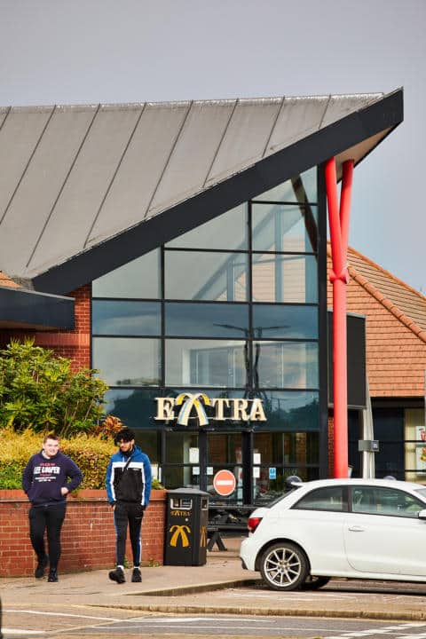 Two individuals standing outside a building with a sign that reads "extra.