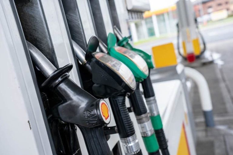 Fuel pumps at a motorway service area, displaying various nozzles in a holder with branding, with a blurred background of the station area.